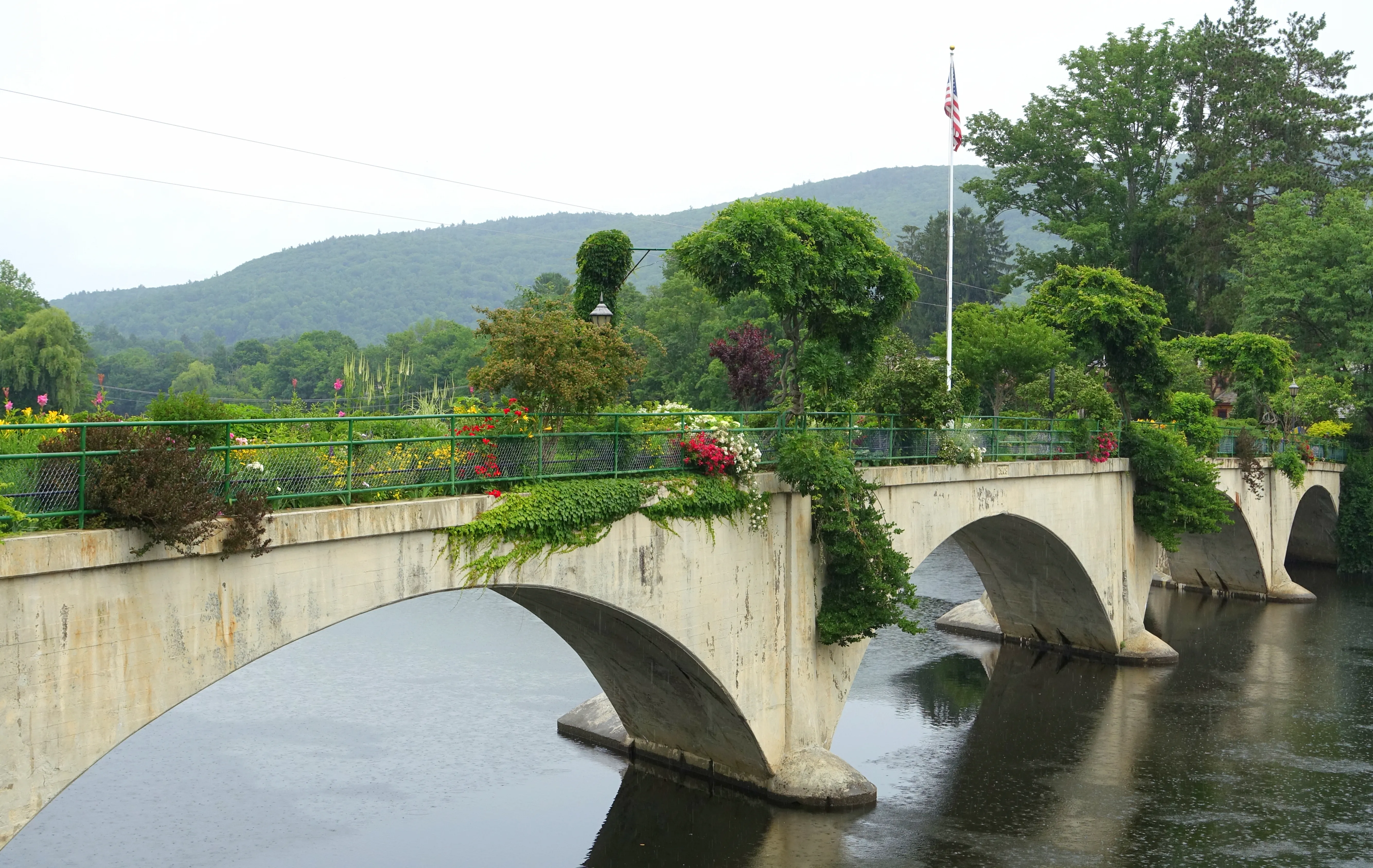 The Bridge of Flowers in Shelburne Falls: a former trolley bridge planted with summer perennials, with a US flag flying at the center.