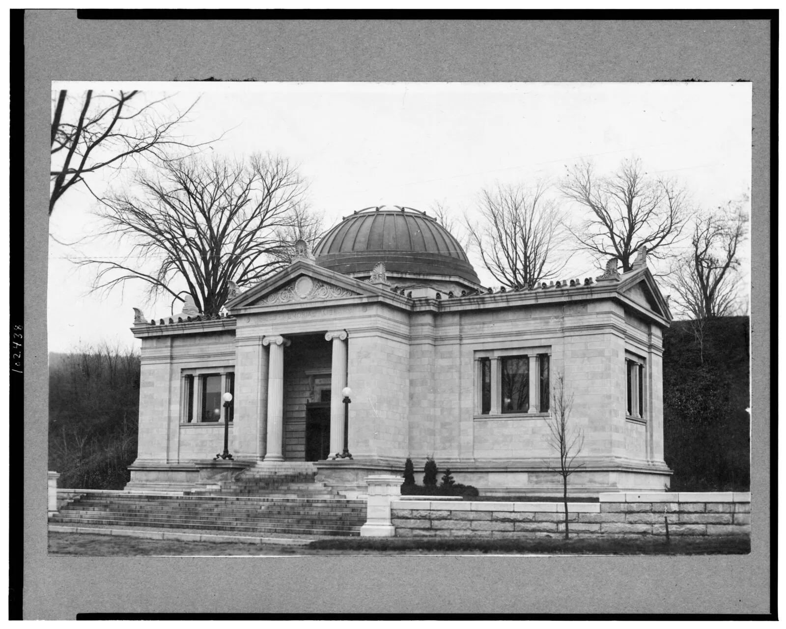 The Field Memorial Library photographed shortly after its completion around 1900: a Beaux-Arts limestone civic building seen in black-and-white from the street, with a low central pediment over a recessed entry flanked by paired Ionic columns, a hemispherical dome rising over the central rotunda, low gable wings extending to either side with tall ground-floor sash windows, ornamental urns at the corners of the parapet, broad stone steps climbing to the entry, and bare deciduous trees in winter behind the building.